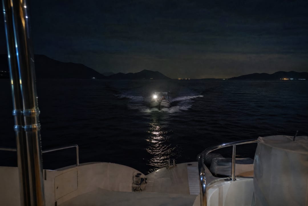 Small fast boat approaching a moored yacht at night