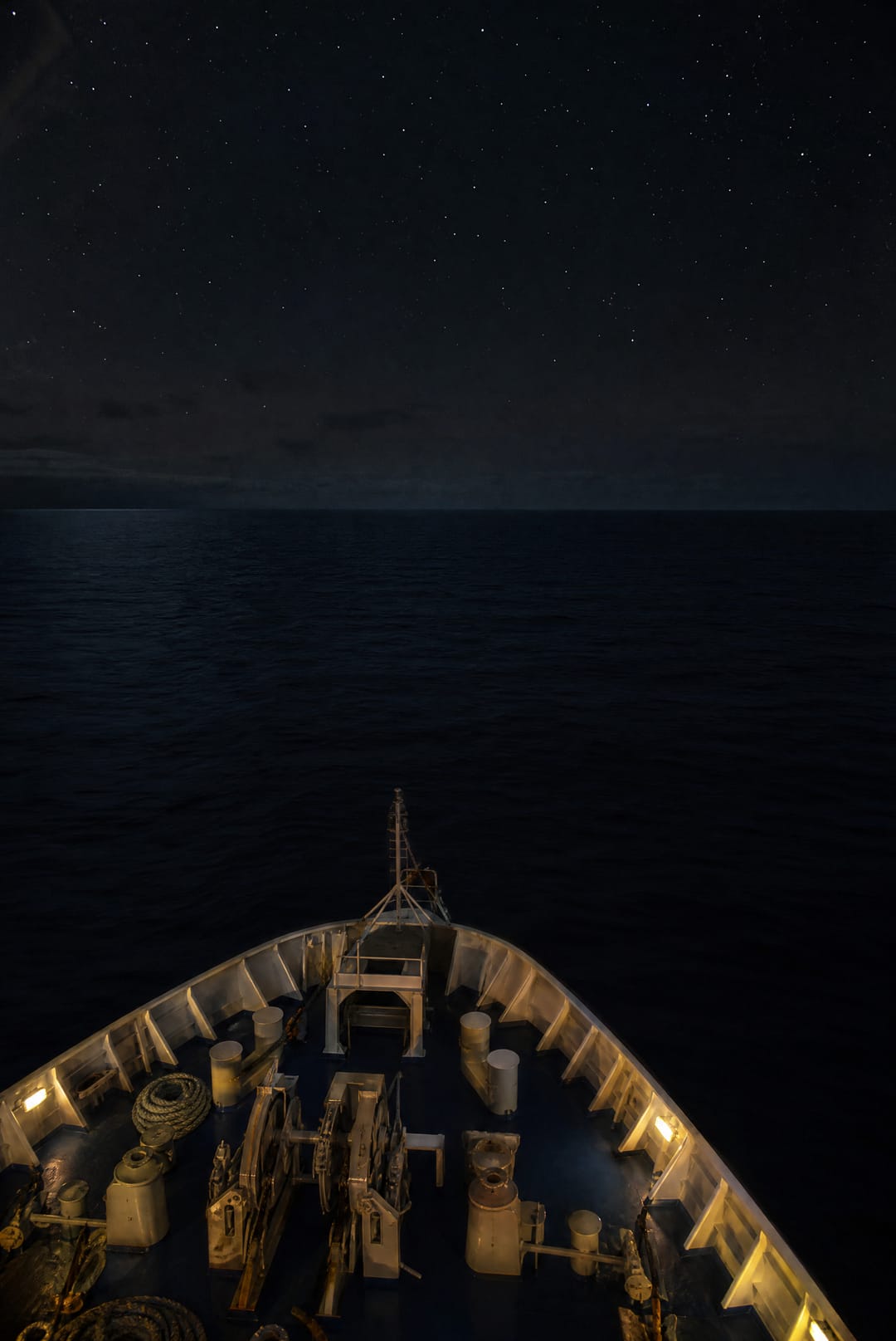 Ship's bow lit by deck lights on a black sea